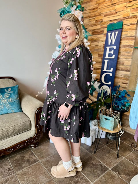 Woman in a black floral dress standing in a living room with decorative elements.