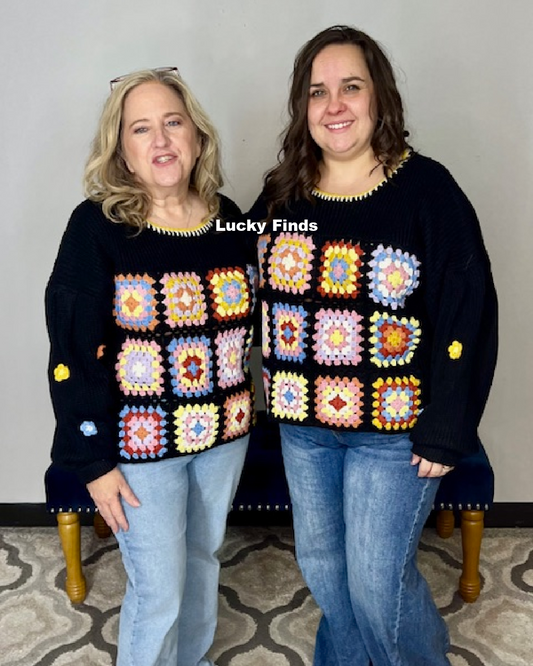 Two women wearing matching black sweaters with colorful square patterns, standing in a room.