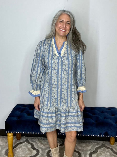 Woman wearing a blue and white patterned dress standing in front of a blue bench.